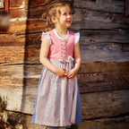 Kinderdirndl in Blush mit rosa geblümter Schürze und blauem Rock mit einem Mädchen vor einem Holzhaus