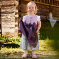 Kinderdirndlbluse und Kinderdirndl fliederfarben mit lila Schürze getragen von einem Kleinkind in einem Garten