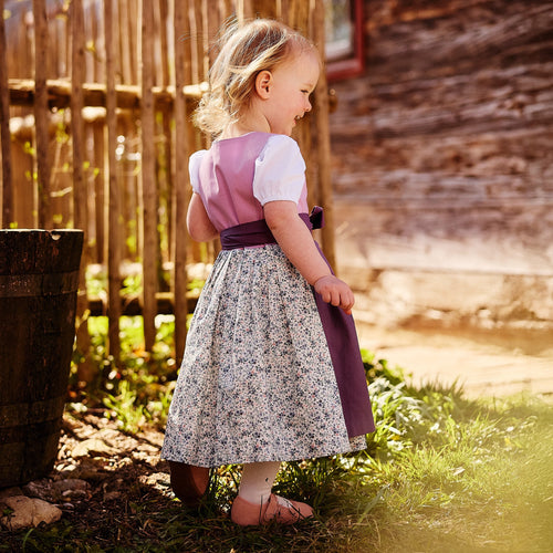 Kinderdirndl in flieder mit lila Schürze und blumigem Rock getragen von einem Mädchen von hinten