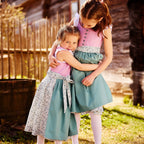 Kinderdirndl fliederfarben mit blumigem Rock und salbeifarbener Schürze, getragen von zwei Geschwister als Geschwisterlook.