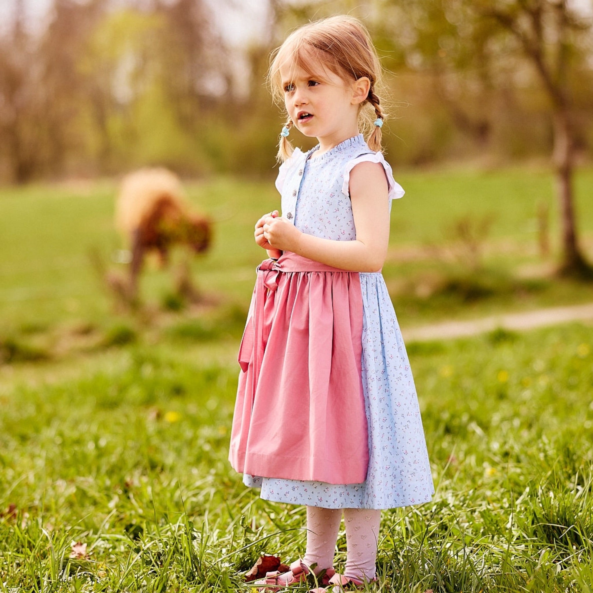 Kinderdirndl in hellblau mit altrosa Schürze handgefertigt in Bayern aus Bio-Baumwolle getragen von einem Mädchen auf einer Wiese