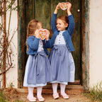 Kinderdirndl in hellblauem Blumenmuster mit blauer Schürze und blauer Kindertrachtenjacke/-strickjacke, getragen von zwei Mädchen mit Lebkuchenherzen in der Hand