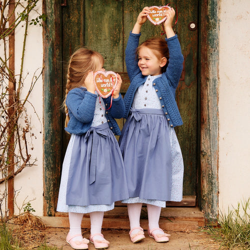 Kinderdirndl in hellblauem Blumenmuster mit blauer Schürze und blauer Kindertrachtenjacke/-strickjacke, getragen von zwei Mädchen mit Lebkuchenherzen in der Hand