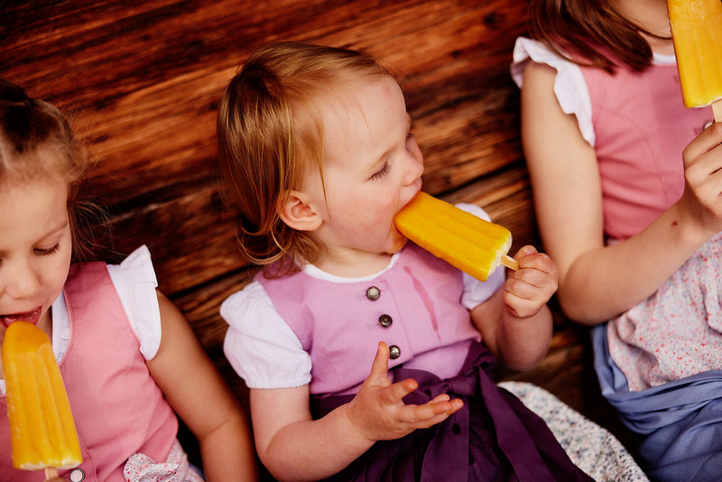 Kinderdirndl getragen von Kindern, die ein geliehenes Dirndl tragen und Eis essen