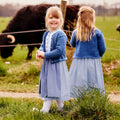 Strickjacke in blau aus Bio-Schurwolle mit Zopfmuster von vorne und hinten getragen von zwei Mädchen auf einer Wiese